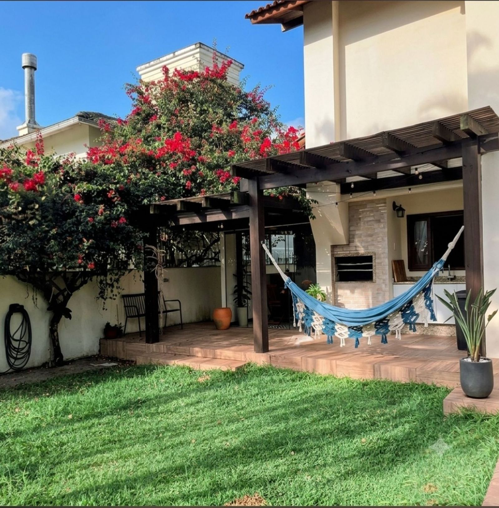 Varanda posterior com churrasqueira integrada ao amplo gramado, piscina e solarium em casa no Parque São Jorge, Itacorubi.