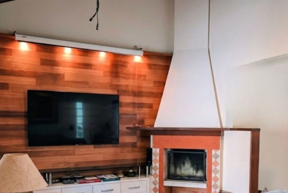 Sala de estar com lareira e painel de madeira em casa a venda no Parque São Jorge, Florianópolis.