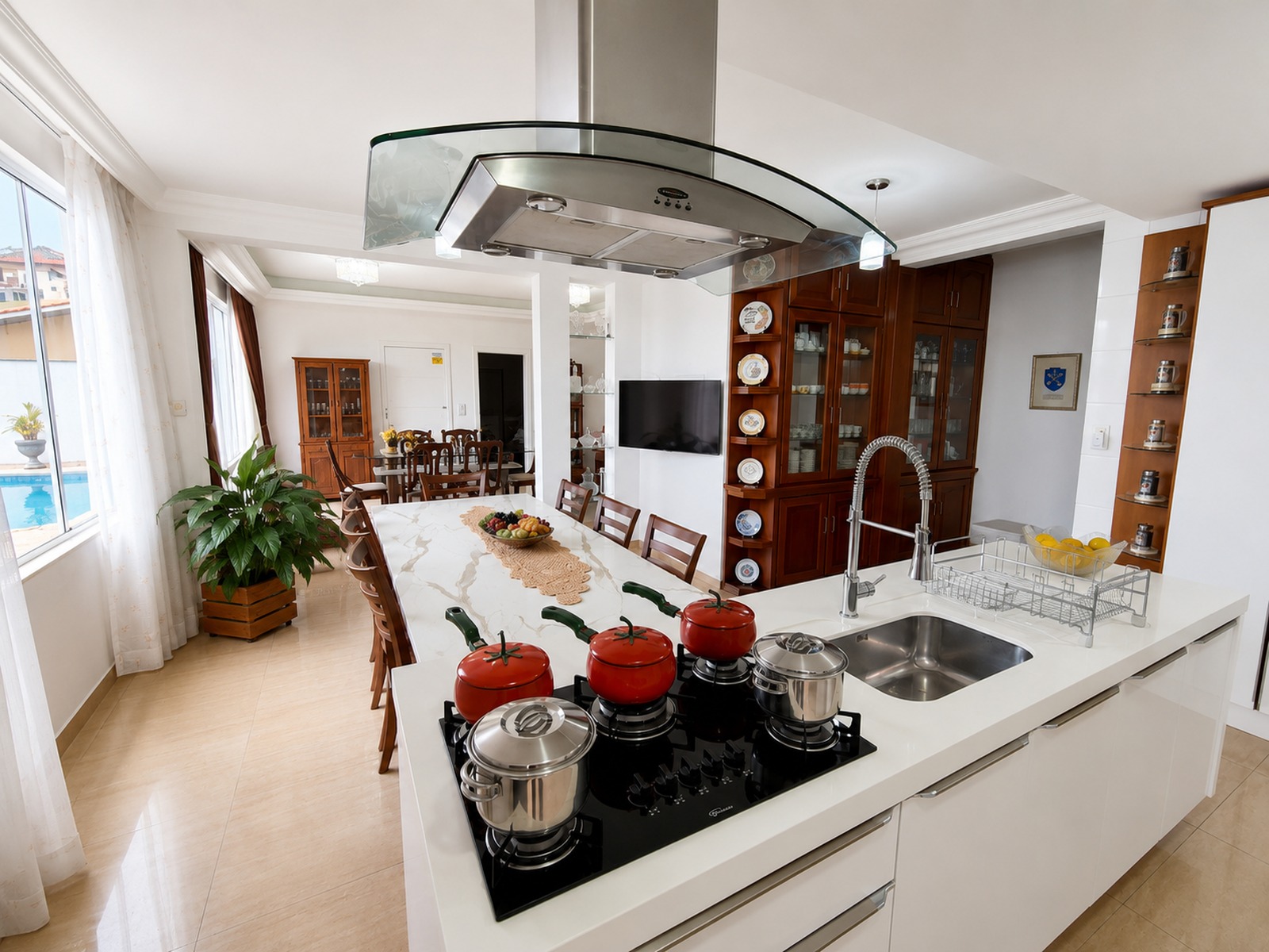 Cozinha americana com ilha, cooktop, coifa e cuba dupla, integrada aos ambientes sociais da casa em Florianópolis.