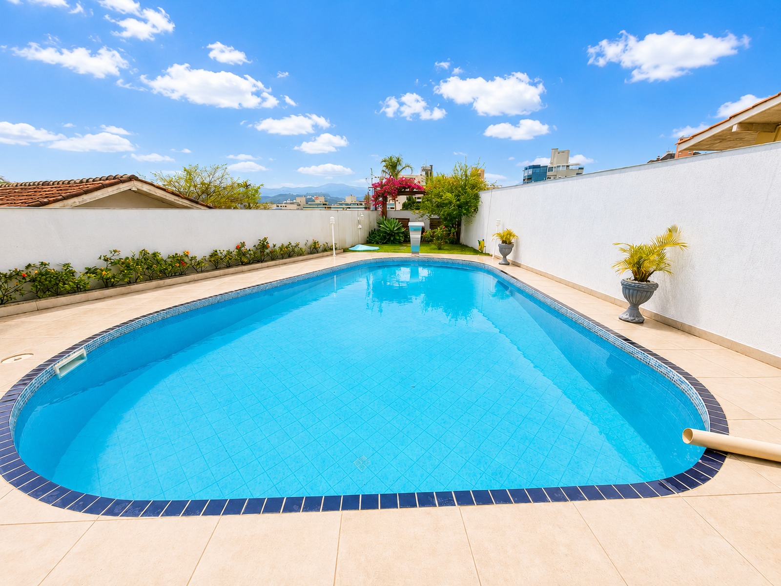 Piscina privativa de grandes dimensões com solarium em porcelanato e jardim ao fundo em residência alto padrão em Florianópolis.