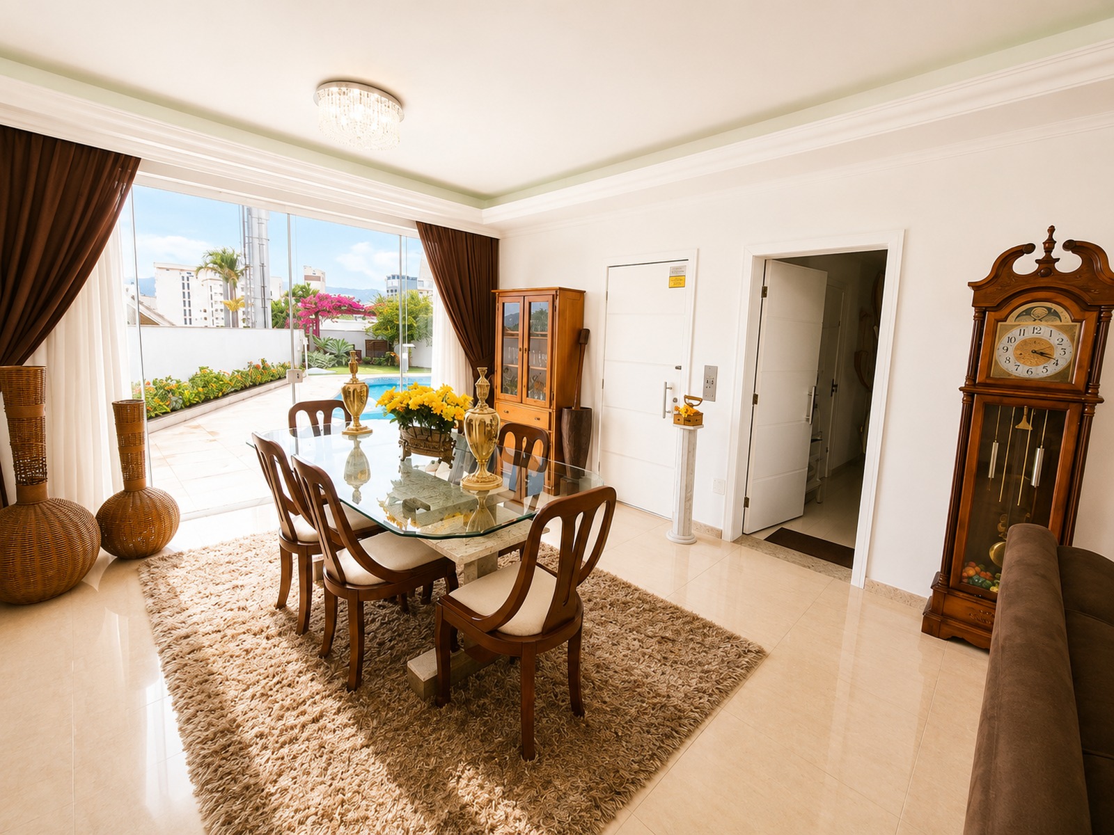 Sala de jantar integrada à área externa, com amplas portas - janelas. Vista para o jardim e piscina da residência.