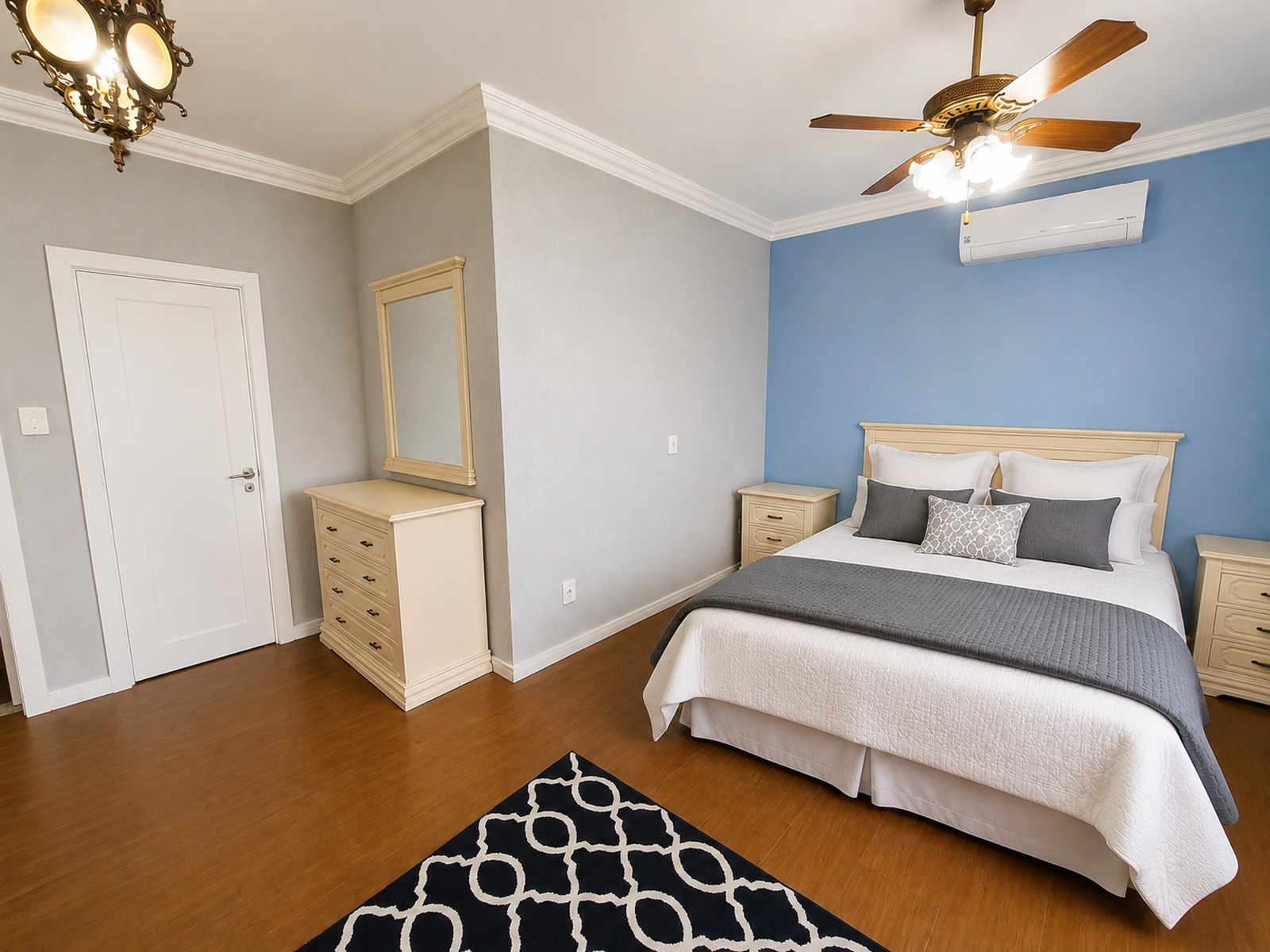 Suíte ampla com piso laminado, ar-condicionado, mobiliário em tons claros e espaço confortável para circulação.